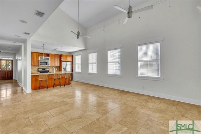 kitchen featuring a breakfast bar, ceiling fan, hanging light fixtures, stainless steel appliances, and decorative backsplash