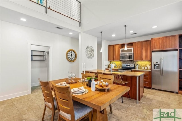 kitchen with sink, decorative light fixtures, appliances with stainless steel finishes, a kitchen island with sink, and decorative backsplash