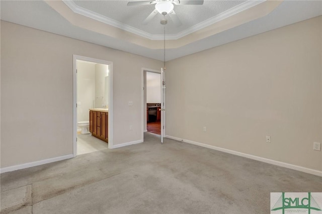 unfurnished bedroom with a raised ceiling, crown molding, light colored carpet, and ensuite bath