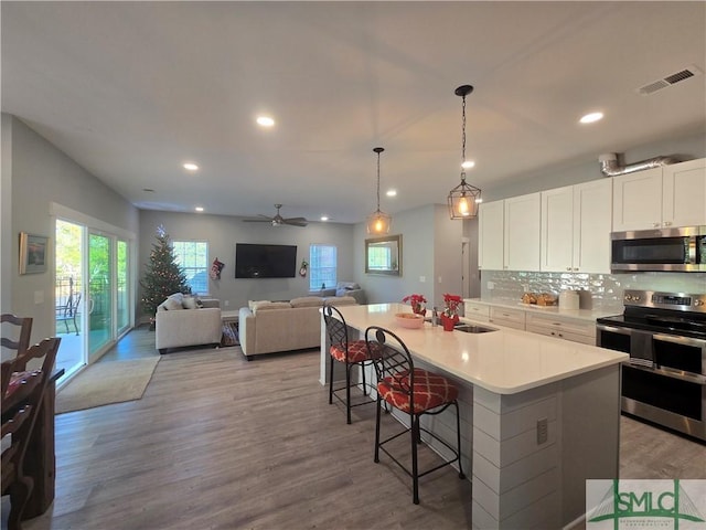 kitchen with a breakfast bar, white cabinetry, decorative backsplash, stainless steel appliances, and a center island with sink