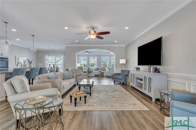 living room featuring crown molding, ceiling fan with notable chandelier, and light hardwood / wood-style floors