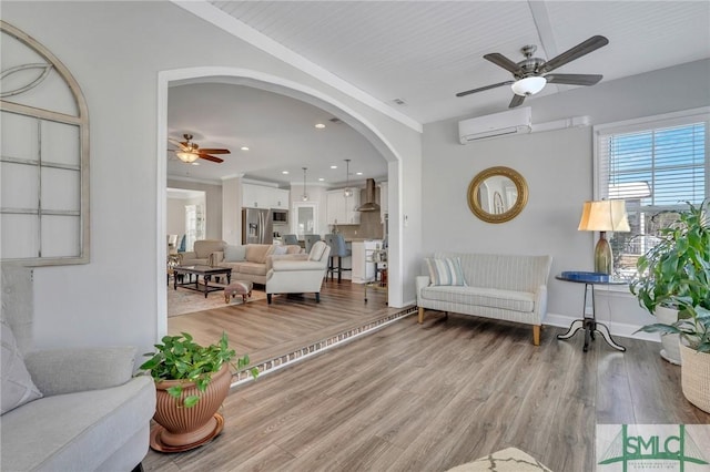 living room featuring wood-type flooring, a wall unit AC, and ceiling fan