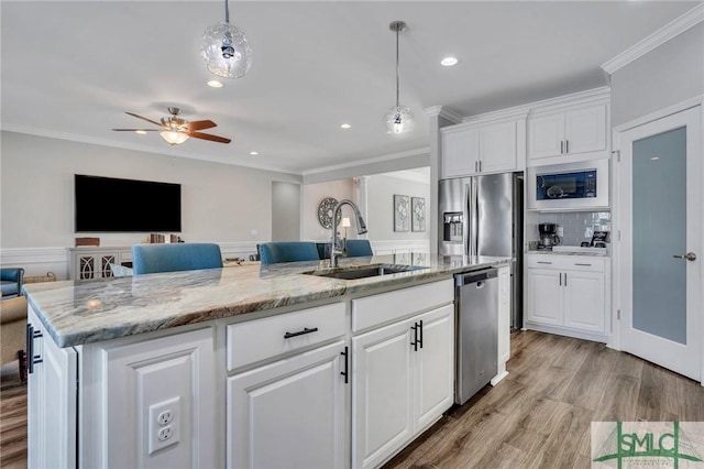 kitchen featuring decorative light fixtures, sink, white cabinets, stainless steel appliances, and a center island with sink