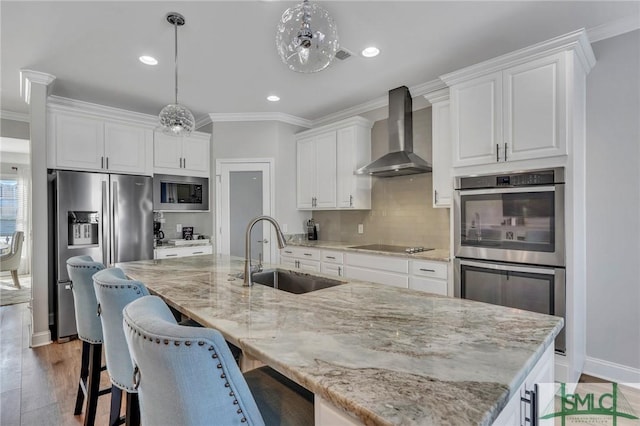 kitchen featuring a spacious island, wall chimney exhaust hood, sink, hanging light fixtures, and white cabinets