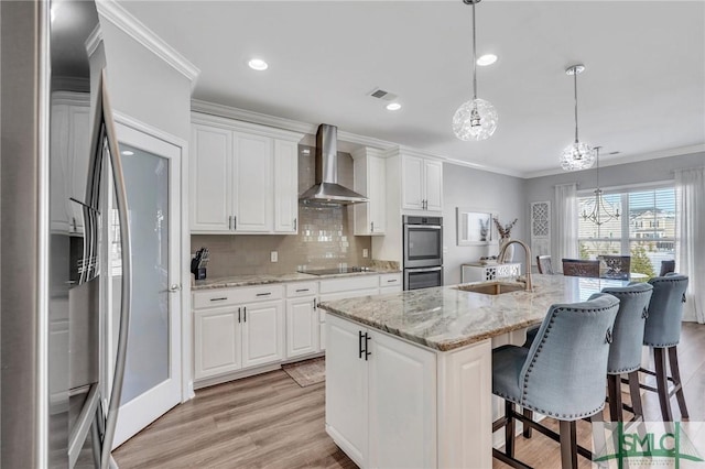 kitchen with white cabinetry, sink, a kitchen island with sink, stainless steel appliances, and wall chimney range hood