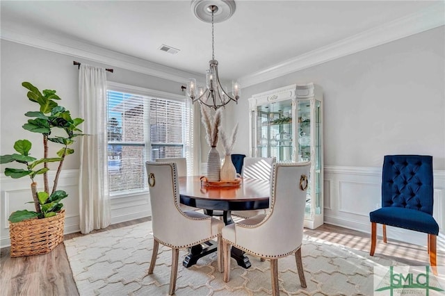 dining space featuring an inviting chandelier, ornamental molding, and light hardwood / wood-style flooring