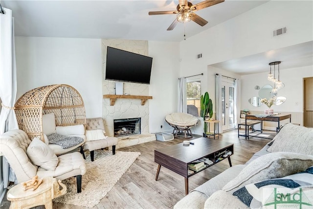 living room with hardwood / wood-style floors, a stone fireplace, high vaulted ceiling, and ceiling fan