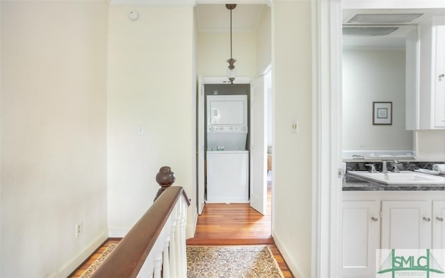 corridor with sink, light hardwood / wood-style flooring, ornamental molding, and stacked washer / dryer