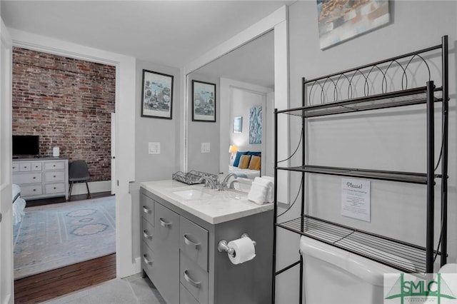 bathroom with brick wall, toilet, and vanity