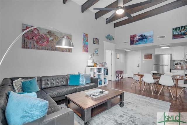 living room featuring beamed ceiling, ceiling fan, wood-type flooring, and a towering ceiling