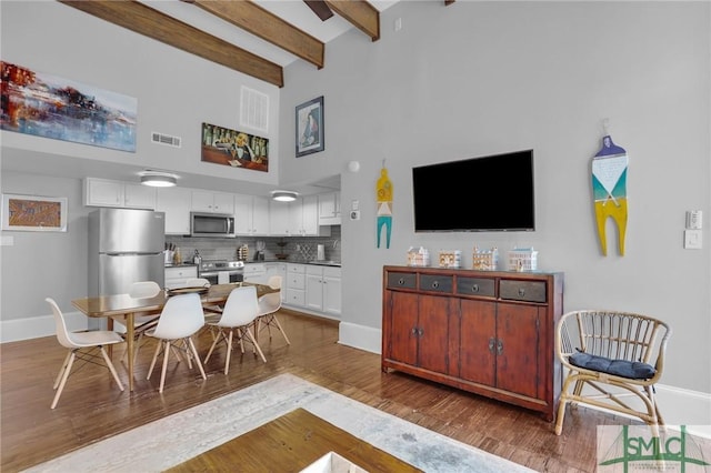 dining area with a towering ceiling, dark wood-type flooring, and beamed ceiling