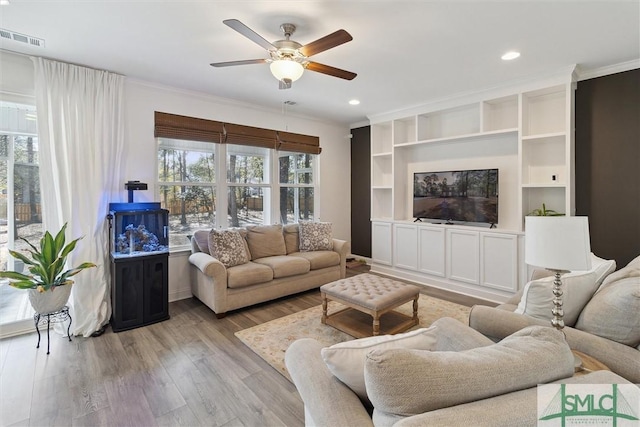 living room featuring built in features, light hardwood / wood-style flooring, ornamental molding, and ceiling fan