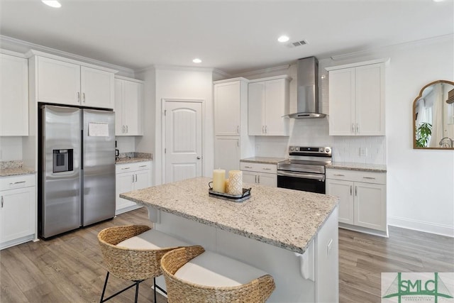 kitchen featuring white cabinets, appliances with stainless steel finishes, a kitchen bar, and wall chimney range hood