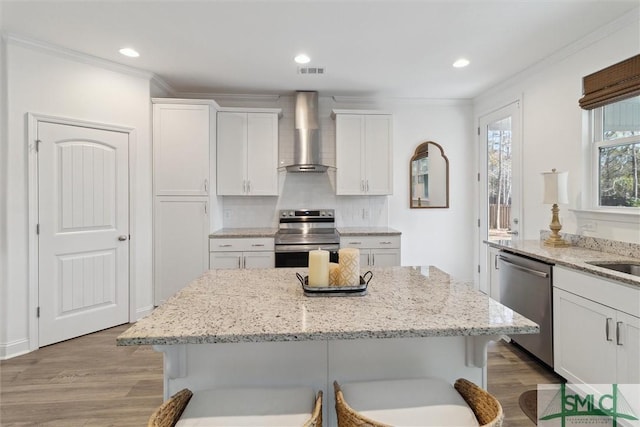 kitchen with wall chimney exhaust hood, a kitchen bar, white cabinetry, light stone counters, and appliances with stainless steel finishes