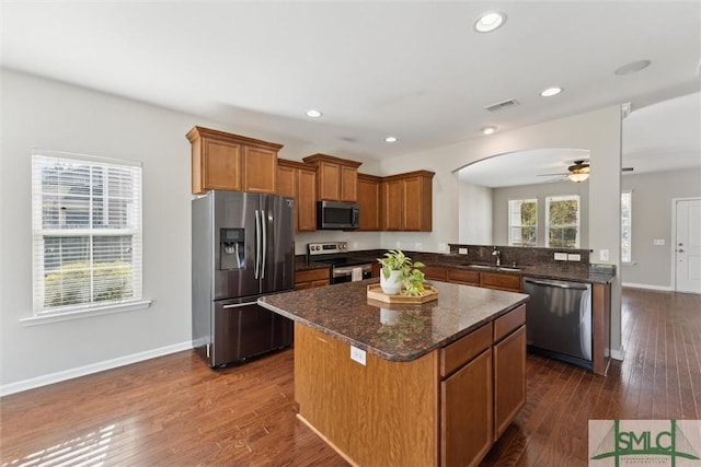 kitchen with sink, appliances with stainless steel finishes, dark hardwood / wood-style floors, kitchen peninsula, and a kitchen island