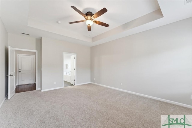 unfurnished bedroom with ensuite bath, a raised ceiling, ceiling fan, and carpet flooring