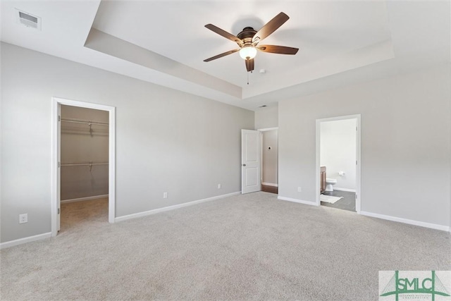 unfurnished bedroom with a walk in closet, light colored carpet, a raised ceiling, ensuite bath, and a closet