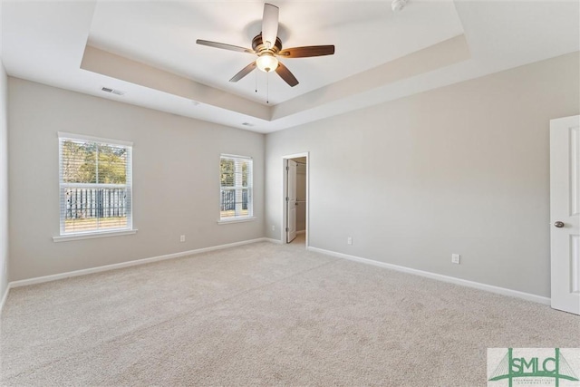 carpeted spare room with a raised ceiling and ceiling fan