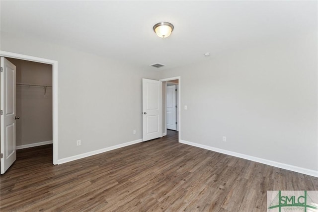 unfurnished bedroom featuring a closet, a walk in closet, and dark hardwood / wood-style floors