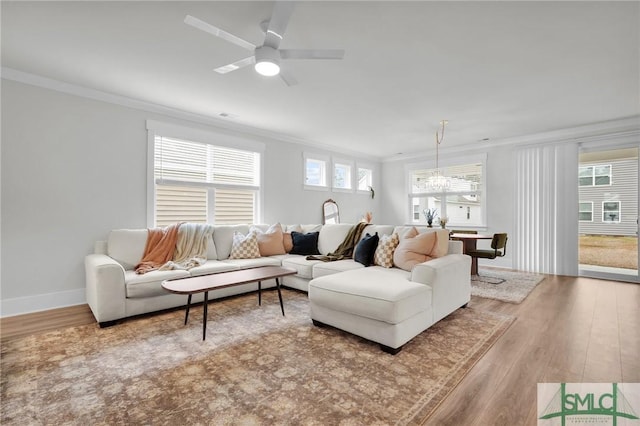 living room with ceiling fan with notable chandelier, crown molding, wood finished floors, and baseboards