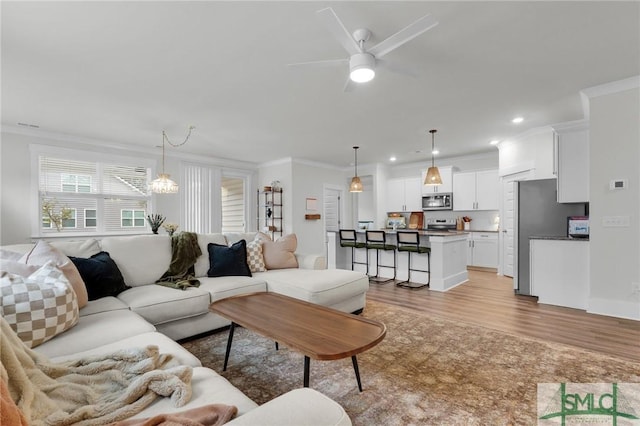 living room with crown molding, ceiling fan, and light wood-type flooring