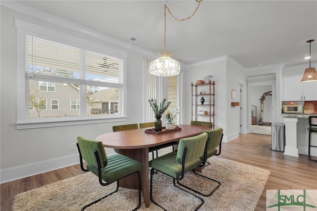 dining room featuring a notable chandelier, baseboards, light wood finished floors, and ornamental molding