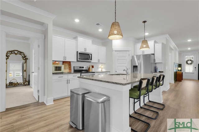 kitchen with white cabinetry, hanging light fixtures, a center island with sink, appliances with stainless steel finishes, and dark stone counters