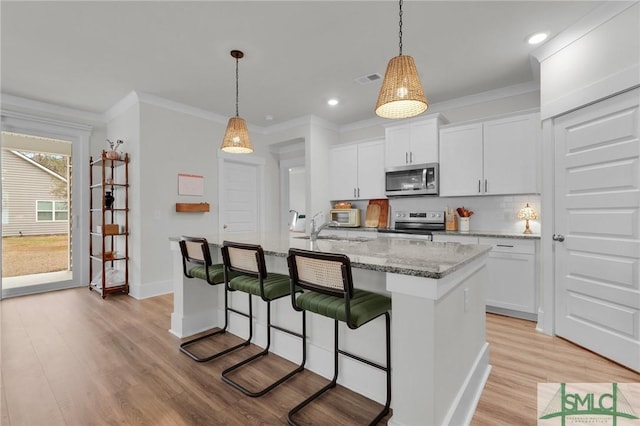 kitchen with pendant lighting, white cabinetry, stainless steel appliances, an island with sink, and light wood-type flooring