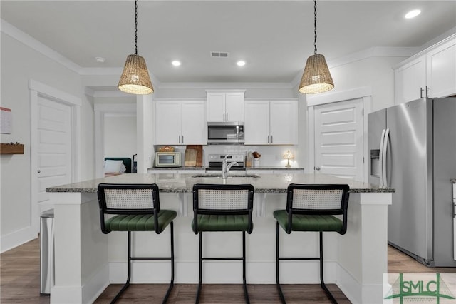 kitchen with stainless steel appliances, a kitchen island with sink, white cabinets, and decorative light fixtures