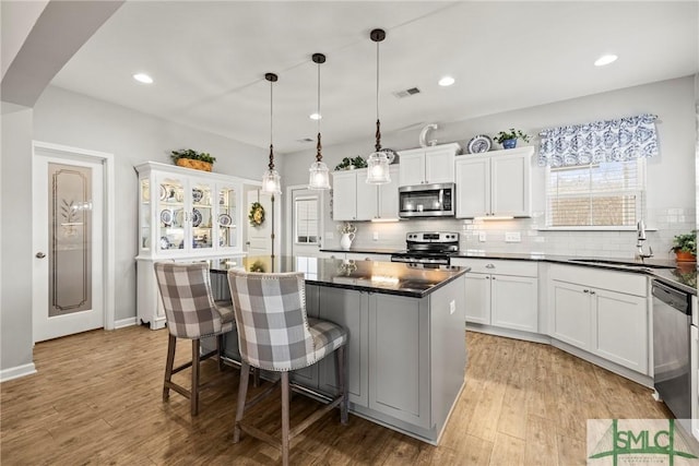 kitchen with appliances with stainless steel finishes, a breakfast bar, white cabinets, hanging light fixtures, and a center island