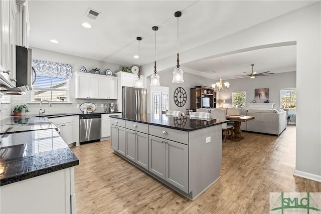 kitchen featuring appliances with stainless steel finishes, hanging light fixtures, backsplash, white cabinets, and a kitchen island