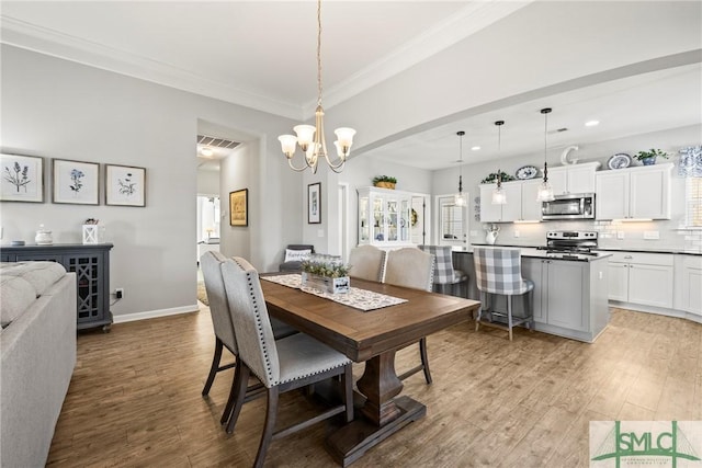 dining area with an inviting chandelier, crown molding, and light hardwood / wood-style floors