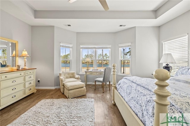 bedroom with a raised ceiling, wood-type flooring, a water view, and ceiling fan