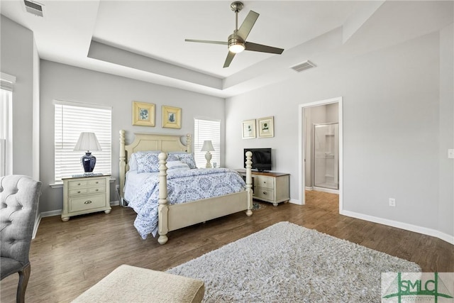 bedroom featuring multiple windows, dark hardwood / wood-style flooring, and a tray ceiling