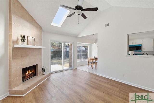 unfurnished living room featuring a skylight, a fireplace, ceiling fan, and light wood-type flooring