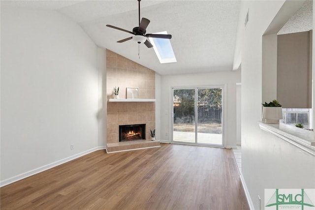 unfurnished living room featuring hardwood / wood-style flooring, lofted ceiling with skylight, a tile fireplace, and ceiling fan