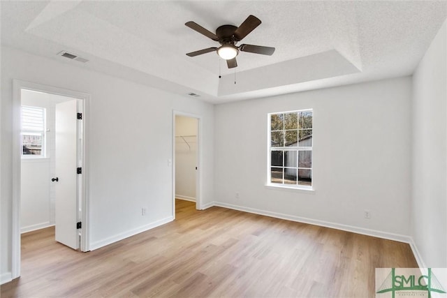 unfurnished bedroom with multiple windows, a tray ceiling, a textured ceiling, and a spacious closet