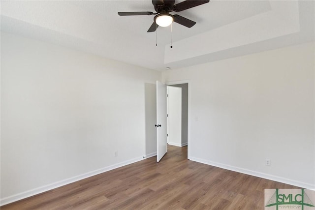 unfurnished room featuring ceiling fan, wood-type flooring, and a raised ceiling