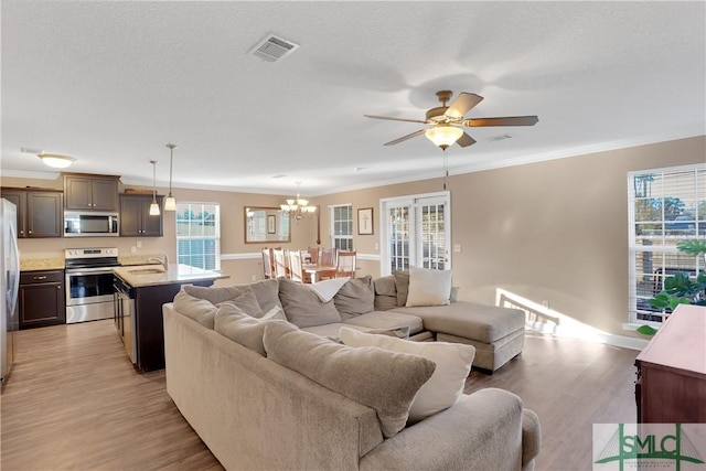 living room featuring ornamental molding, plenty of natural light, ceiling fan with notable chandelier, and light wood-type flooring