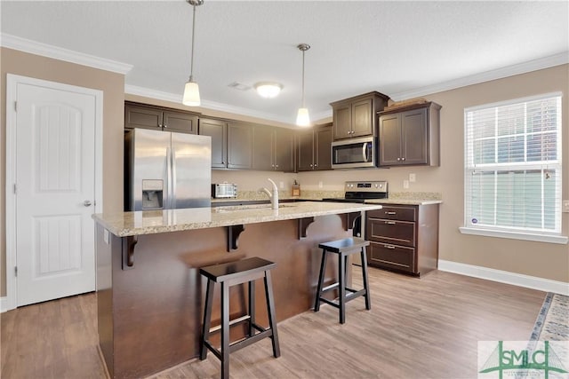 kitchen with sink, light stone counters, ornamental molding, pendant lighting, and stainless steel appliances