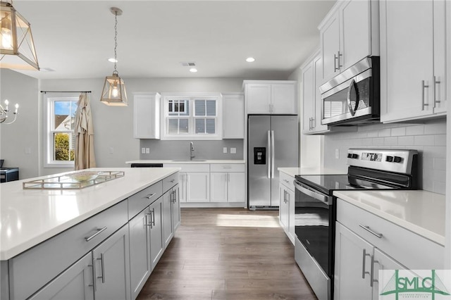 kitchen with hanging light fixtures, appliances with stainless steel finishes, dark hardwood / wood-style floors, white cabinets, and backsplash