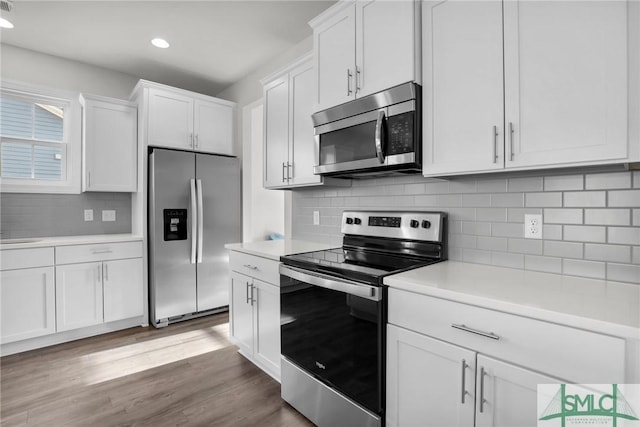 kitchen featuring sink, hardwood / wood-style flooring, white cabinetry, stainless steel appliances, and tasteful backsplash