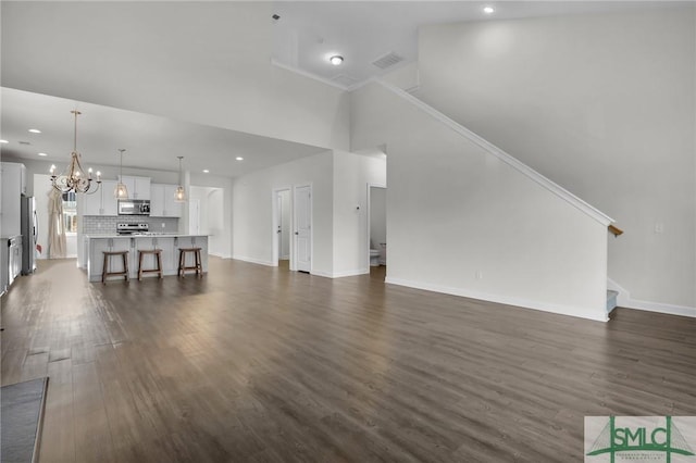 unfurnished living room with an inviting chandelier, a towering ceiling, and dark hardwood / wood-style floors