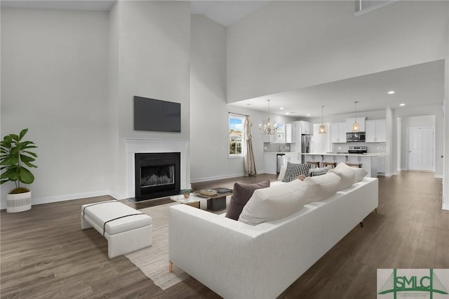 living room featuring a notable chandelier, a towering ceiling, and dark wood-type flooring