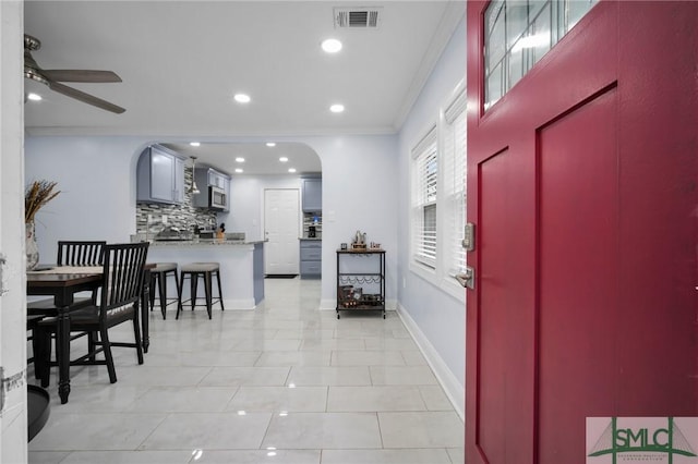 entryway with arched walkways, a ceiling fan, baseboards, visible vents, and crown molding