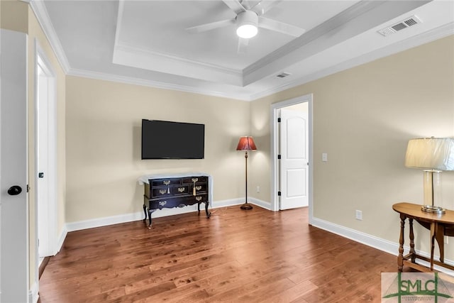 interior space with ceiling fan, ornamental molding, a raised ceiling, and hardwood / wood-style floors