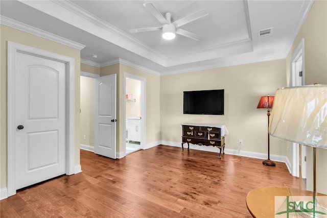 living room featuring a raised ceiling, wood-type flooring, ornamental molding, and ceiling fan