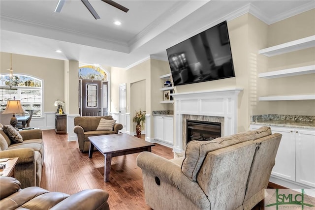 living room featuring crown molding, a high end fireplace, built in features, and light wood-type flooring