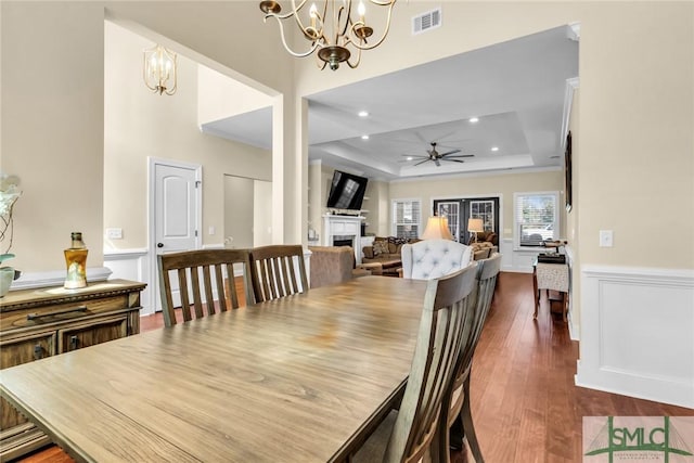 dining room with dark hardwood / wood-style flooring, a tray ceiling, and ceiling fan with notable chandelier