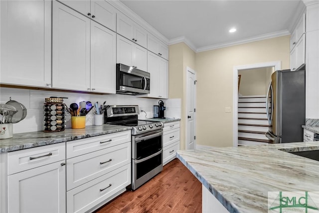 kitchen featuring white cabinetry, backsplash, stainless steel appliances, crown molding, and light stone countertops